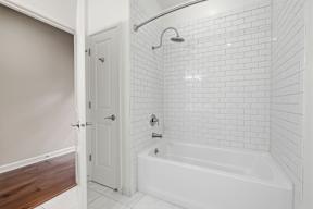 A white tiled bathroom with a white tub and a white door.