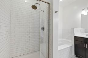 A white tiled bathroom with a shower and a bathtub.