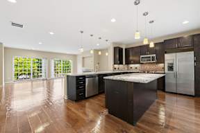 A modern kitchen with dark wood floors and stainless steel appliances.
