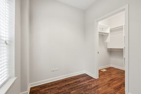 A room with white walls and wooden floors with a window on the left.