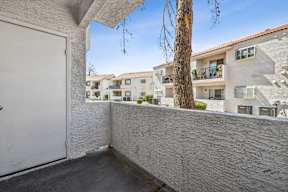 A white door is on the left of a balcony with a tree in the background.