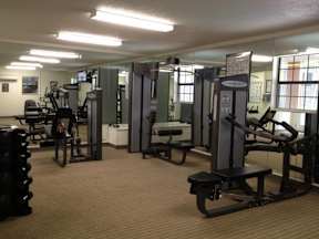 A gym with a variety of equipment including a squat rack, a leg press machine, and a bench press.