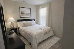 A bedroom with a large bed and a nightstand with a lamp and plant.