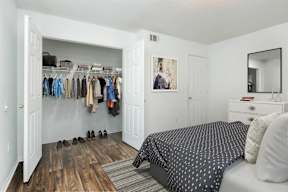 A bedroom with a bed, dresser, and a closet with clothes.