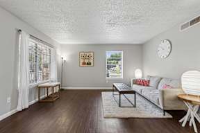 A living room with a grey couch, a coffee table, and a clock on the wall.