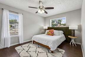 A bedroom with a bed, a ceiling fan, and a window with white curtains.