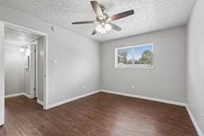 A room with a ceiling fan and a window showing a view of trees.