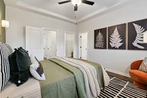 A bedroom with a bed, pillows, a blanket, a chair, and a ceiling fan.