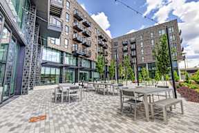 A patio with tables and chairs is surrounded by modern buildings.