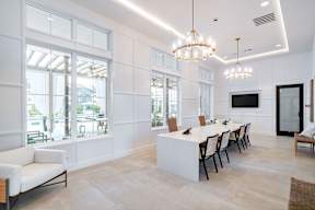 a long white table with chairs in a room with large windows