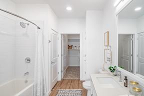 a bathroom with a white tub and shower and a white sink with a mirror above it