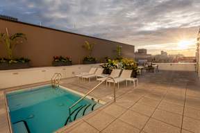 A sunset view of a pool area with chairs and plants.