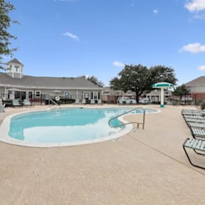 A large outdoor swimming pool with a diving board and a small building in the background.