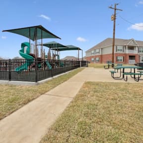 A playground with a green slide and a building in the background.