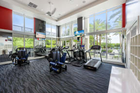 a gym with cardio equipment and large windows