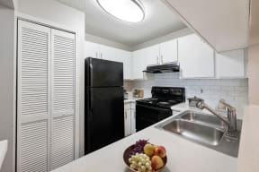 a kitchen with white cabinets and black appliances and a bowl of fruit on the counter