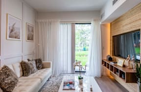 A living room with a white couch and a coffee table in front of a window with curtains.