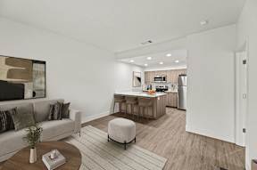 A modern living room with a grey sofa, a coffee table, and a kitchen in the background.