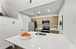 A kitchen with a white countertop and a bowl of oranges on it.