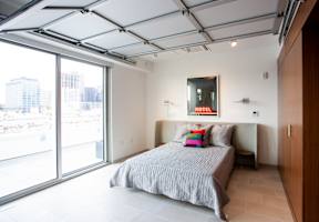 A bedroom with a bed, pillows, and a window overlooking a cityscape.