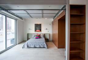 A bedroom with a bed, a window, and a wooden shelf.