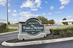 A sign for The Trails of Dickson Apartment Homes is displayed in front of a road.