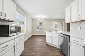 A kitchen with white cabinets and brown flooring.