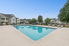 A large swimming pool surrounded by a concrete floor and residential buildings.