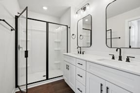 A white bathroom with a black shower door and a white sink.