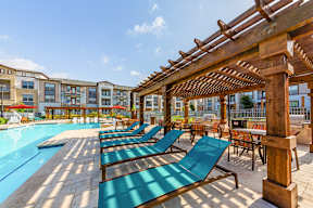 A poolside area with sun loungers and a wooden pergola.