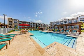 A large outdoor swimming pool surrounded by sun loungers and umbrellas.