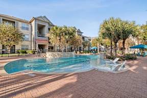 A swimming pool surrounded by a brick patio and palm trees.