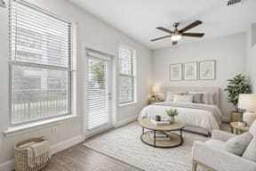 A bedroom with a bed, a chair, a table, and a ceiling fan.