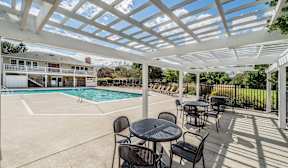 A patio with a table and chairs overlooking a pool.