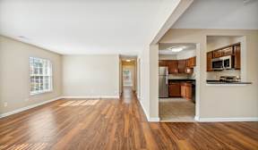A spacious living room with hardwood floors and a kitchen area in the background.