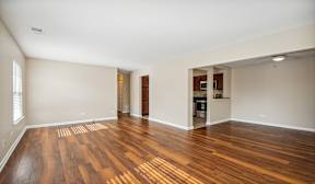 A room with wooden flooring and a kitchen area in the background.