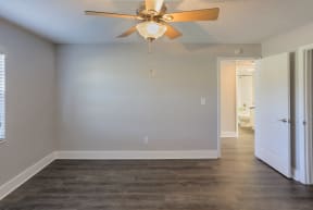 an empty living room with a ceiling fan and a door to a bathroom