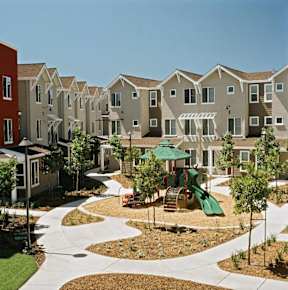A playground area with a green slide and a red slide in the middle of a courtyard surrounded by apartment buildings.