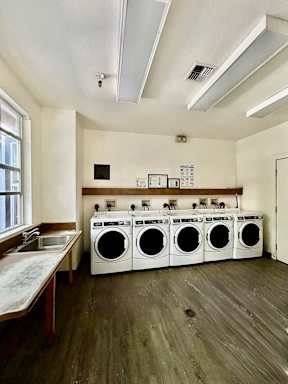 A laundry room with a row of washing machines and a sink.
