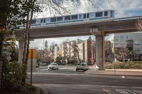 A train is crossing a bridge over a road with cars.