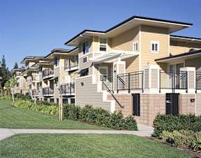 A row of townhouses with balconies and a green lawn in front.