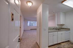A hallway with a carpeted floor and white walls leading to a kitchen area.