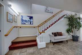 A staircase with a red carpeted landing and a white couch with a pillow beside it.