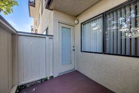 A white door is on the left side of a patio with a red floor.