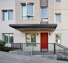 A white house with a red door and a black railing.