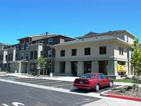 A red car is parked in a parking lot in front of a building.
