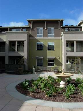 A courtyard with a fountain and plants in front of apartment buildings.