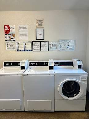 Three front loading washing machines are in a laundry room with paperwork on the wall.