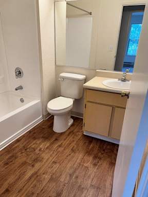 A white toilet sits in a bathroom with wooden floors.