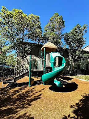 A playground with a green slide and a brown sandbox.